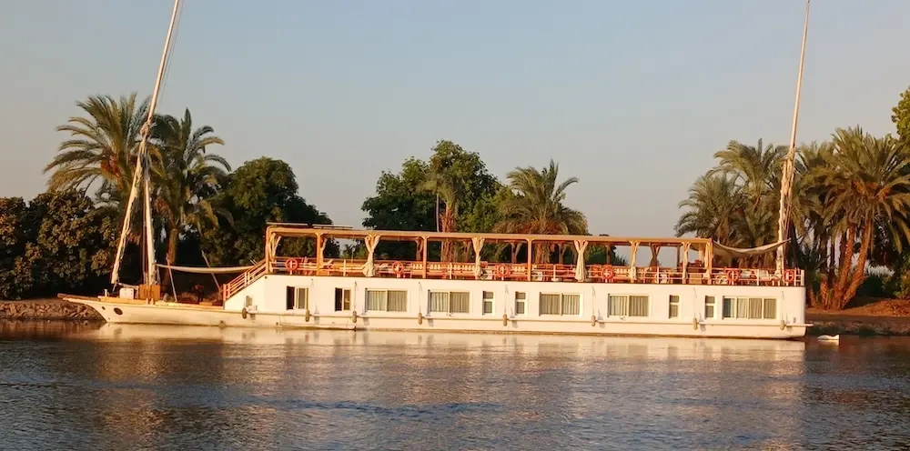 Dahabiya sailing boat moored on the Nile at sunset with two tall masts and an open upper deck