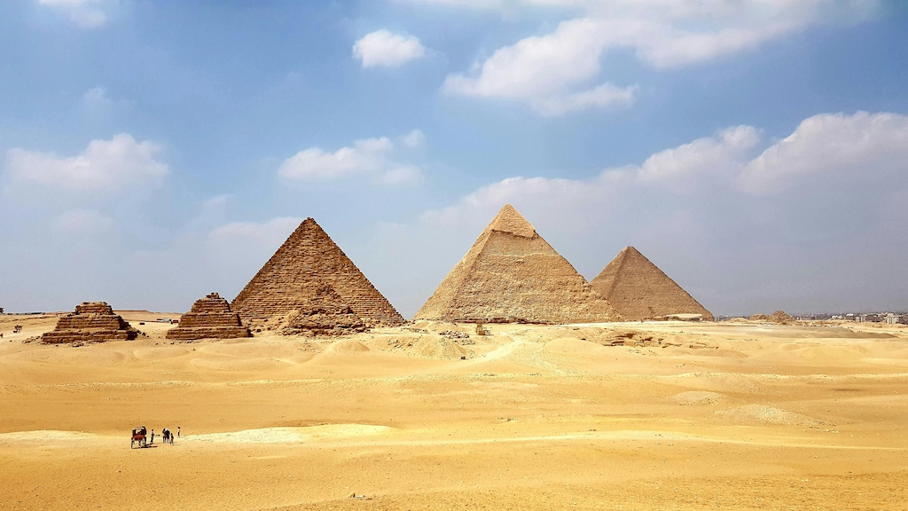 Wide landscape view of the three Pyramids of Giza rising from the desert under a clear blue sky — Plan a trip to Egypt 