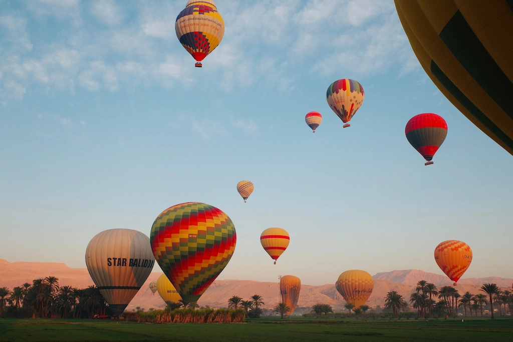 Fleet of hot air balloons drifting over Luxor's palm groves at sunrise