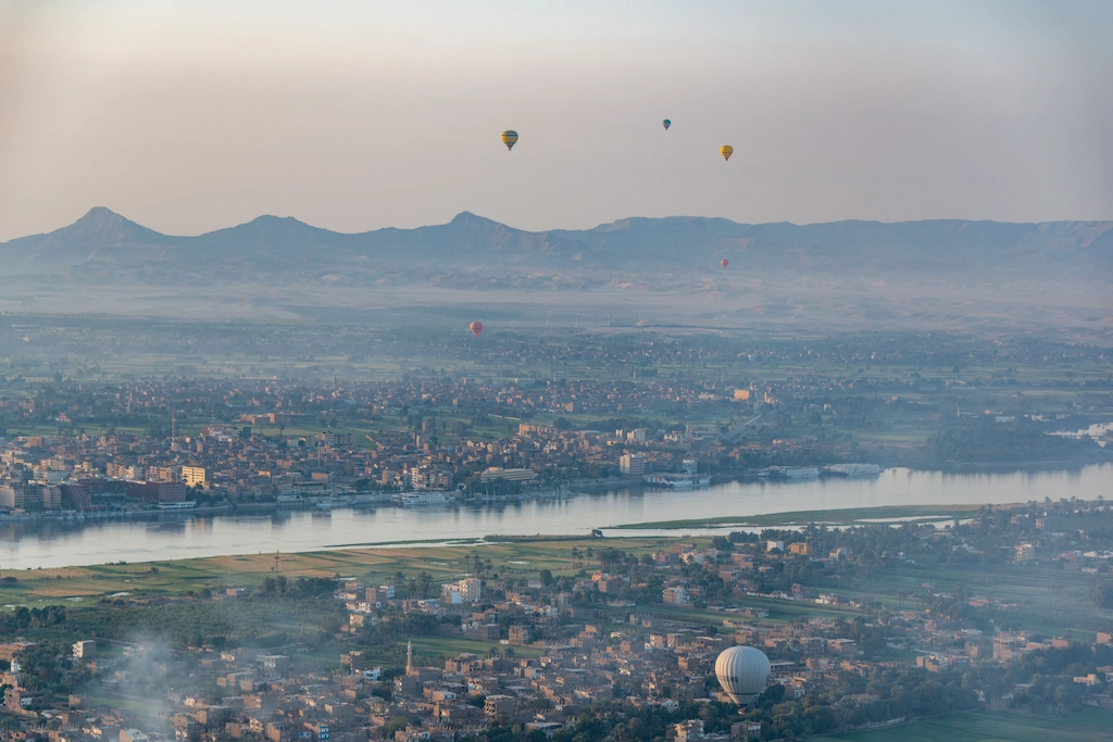Aerial hot air balloon view of the Nile River and Luxor cityscape framed by desert mountains