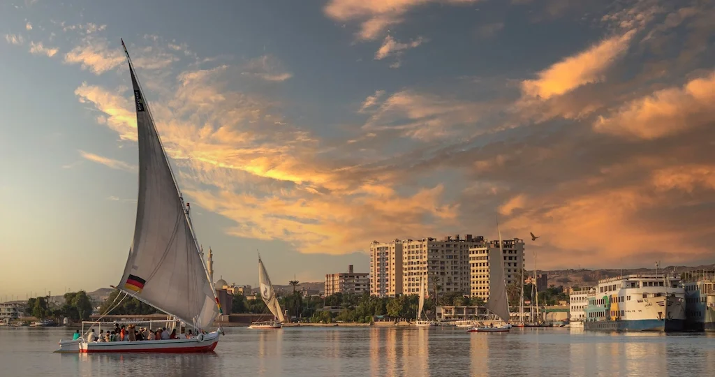 Traditional felucca sailboat at sunset near a Nile cruise ship in Aswan