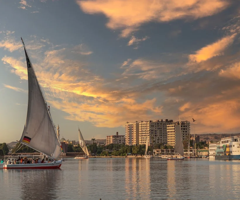 Traditional felucca sailboat at sunset near a Nile cruise ship in Aswan