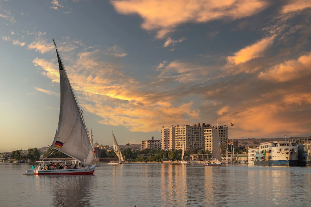 Traditional felucca sailboat at sunset near a Nile cruise ship in Aswan - Best Egypt Tours with Nile Cruise