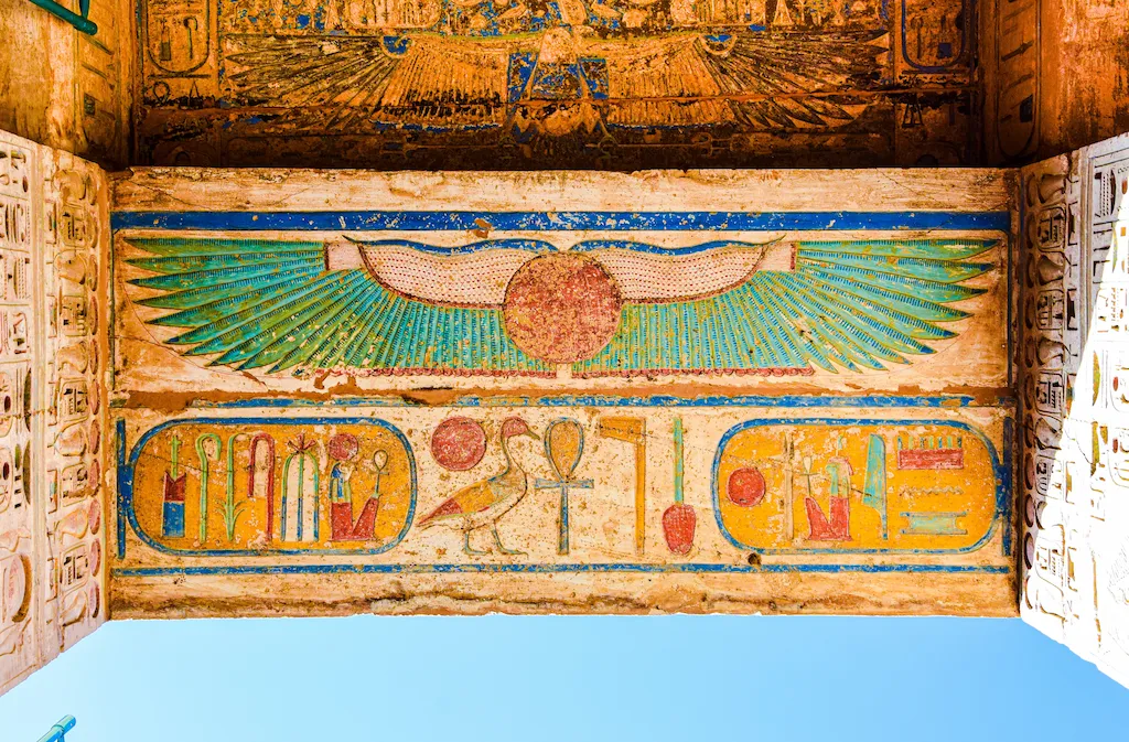 Winged sun disc of Ra and painted hieroglyphs at Medinet Habu — pharaohs "tagged" gods in every scene for divine credibility - social media in ancient egypt