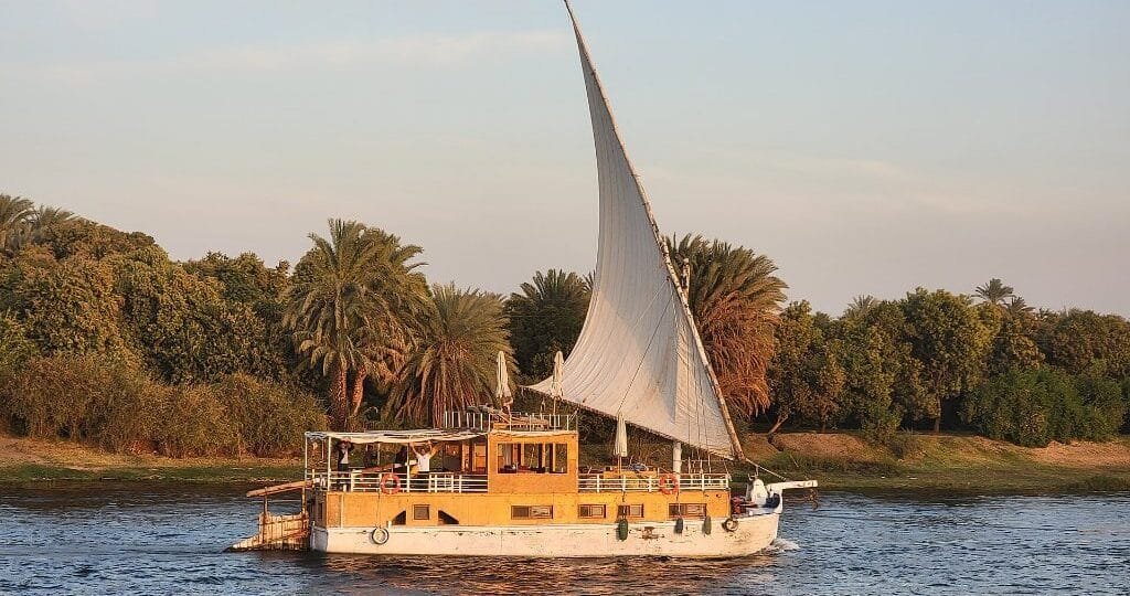 Dahabiyah vs Nile cruise - traditional dahabiya under full sail on the Nile at golden hour