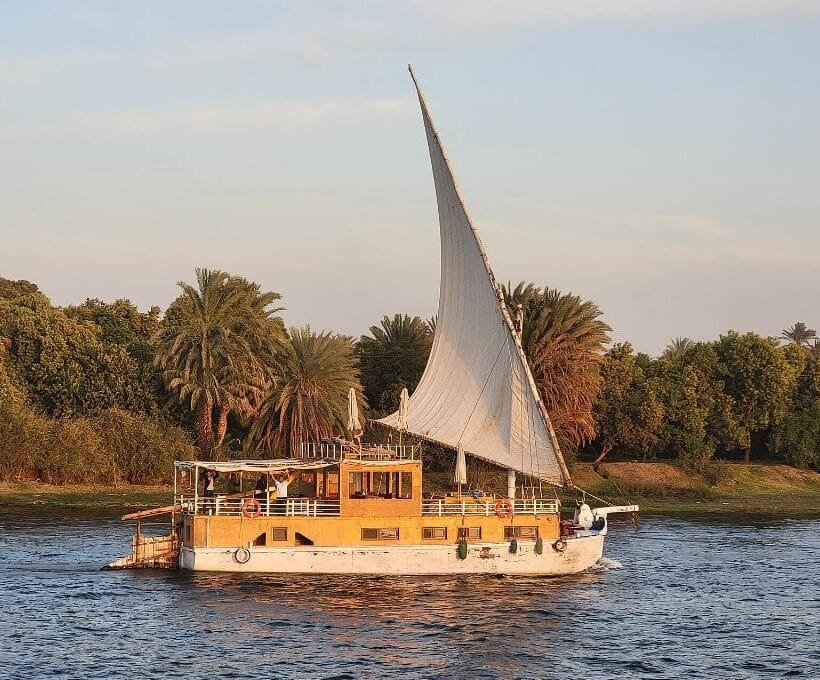 Dahabiyah vs Nile cruise - traditional dahabiya under full sail on the Nile at golden hour