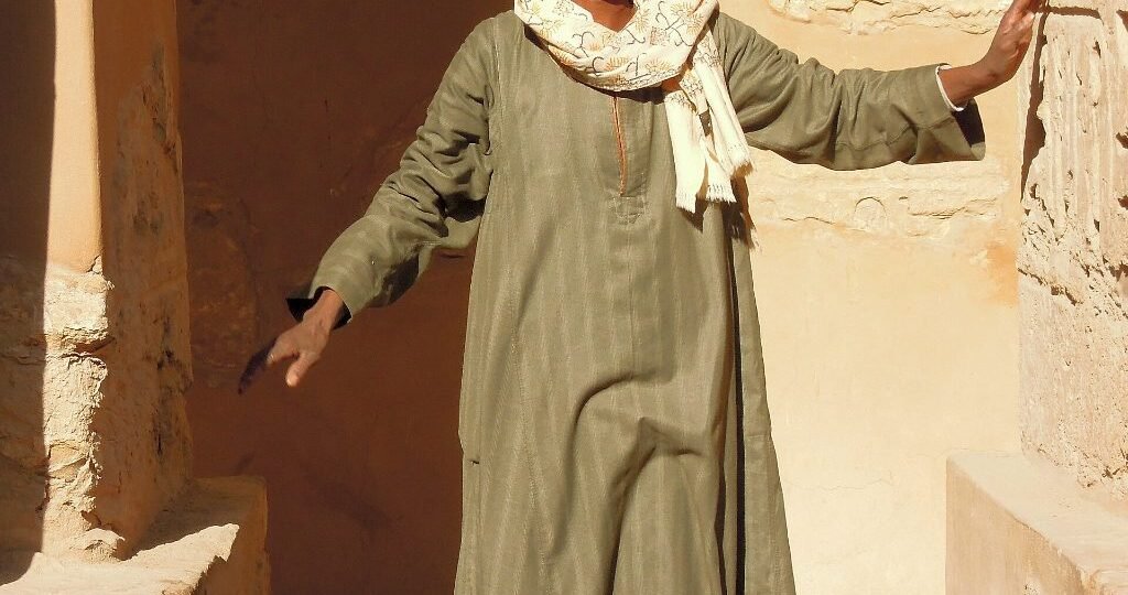 Egyptian traditional clothes: a man in an olive-green jellabiya standing in a stone doorway in Luxor